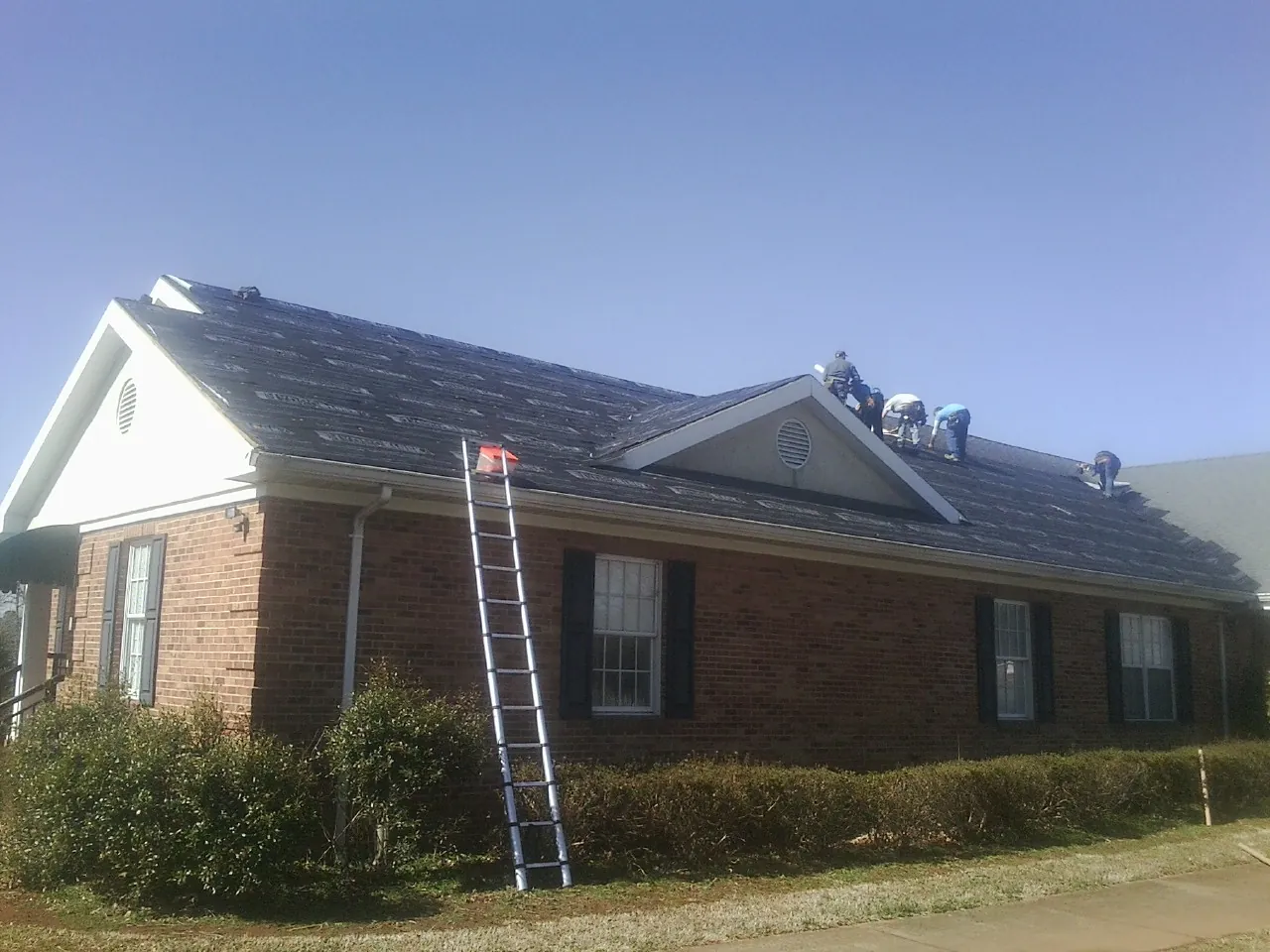 Crew tearing shingles off a brick ranch roof with a ladder set — Metal Roof Repair work by our crew in Summit