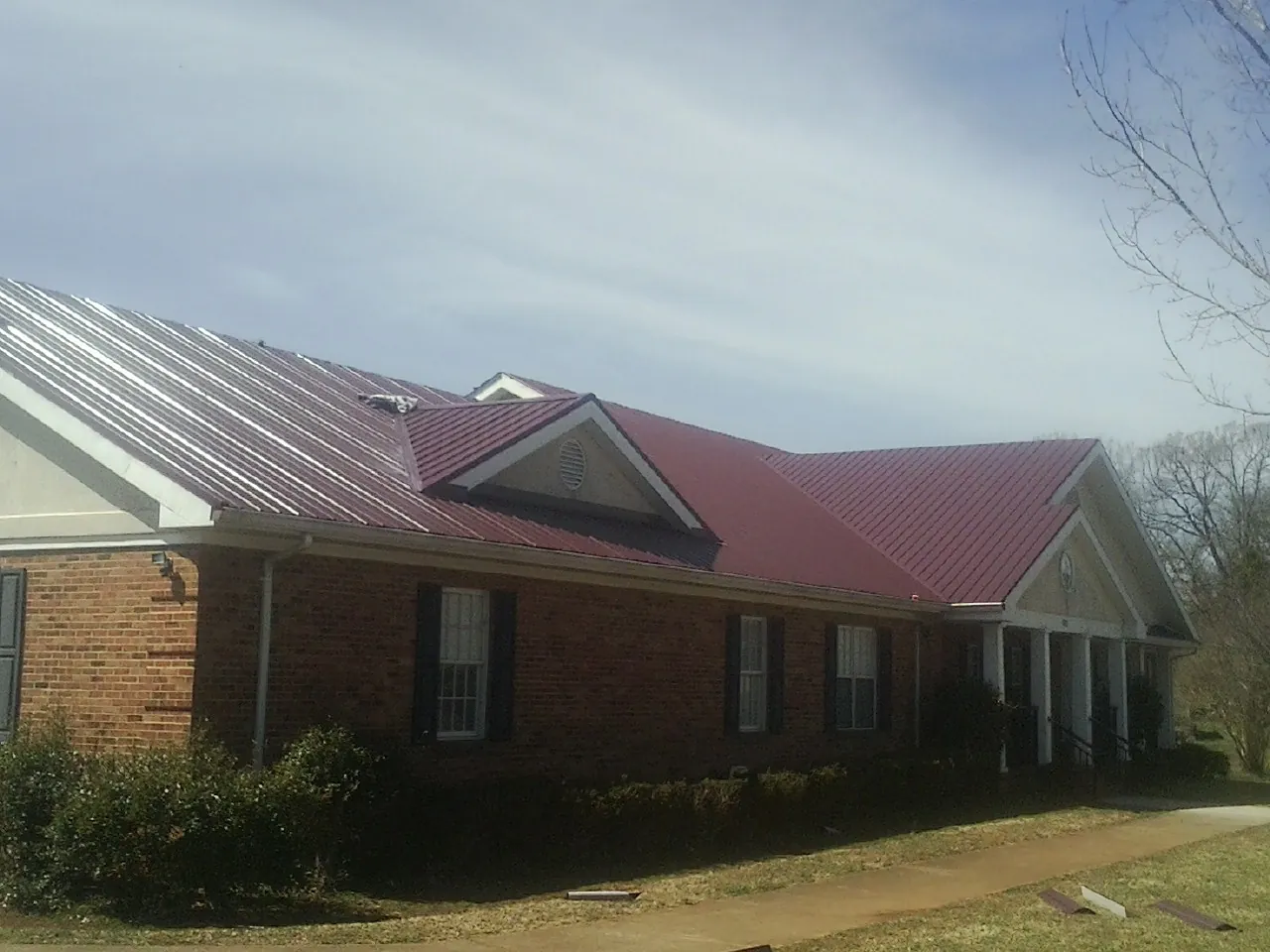 Red metal roof with gabled entries on a long brick building, from a Hail Damage Roof Repair job in Summit