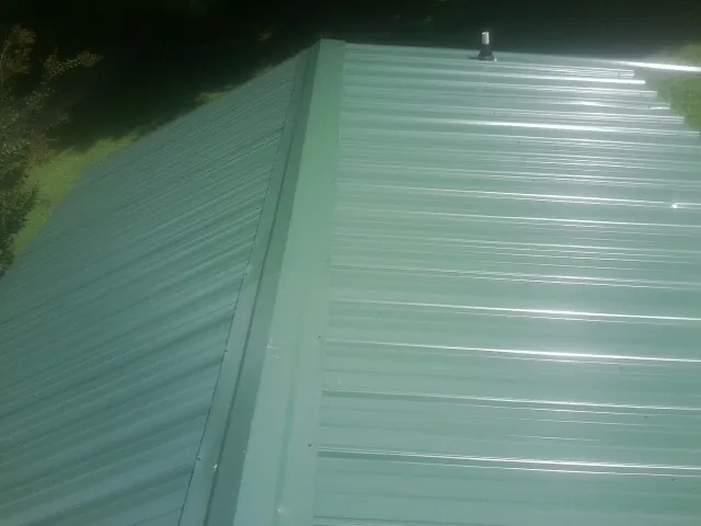 New green metal panels meeting at the ridge of a roof — Flat Roof Repair work by our crew in Summit
