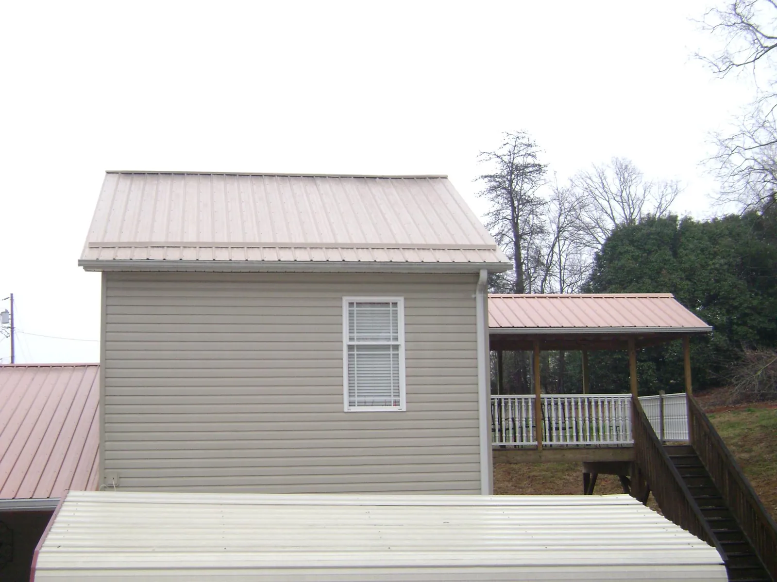 Tan metal roofs on a two story addition and attached porch, from a Roof Replacement job in Summit